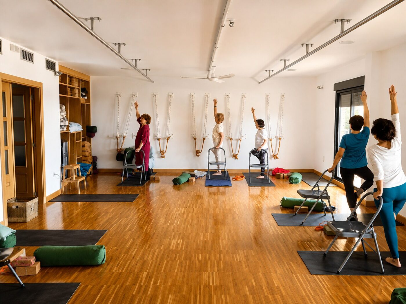 Practicantes de yoga adaptado de pie sobre sillas, con apoyo de las cuerdas de pared, brazo en alto