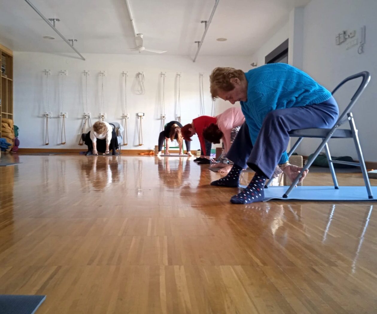 Practicantes de yoga adaptado con apoyo de sillas, en una flexión hacia delante