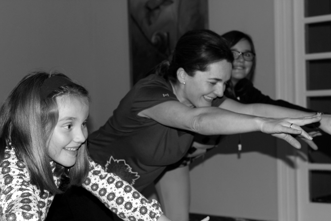Alumnos apoyados en sillas, con un brazo levantado, en la primera clase de yoga adaptado