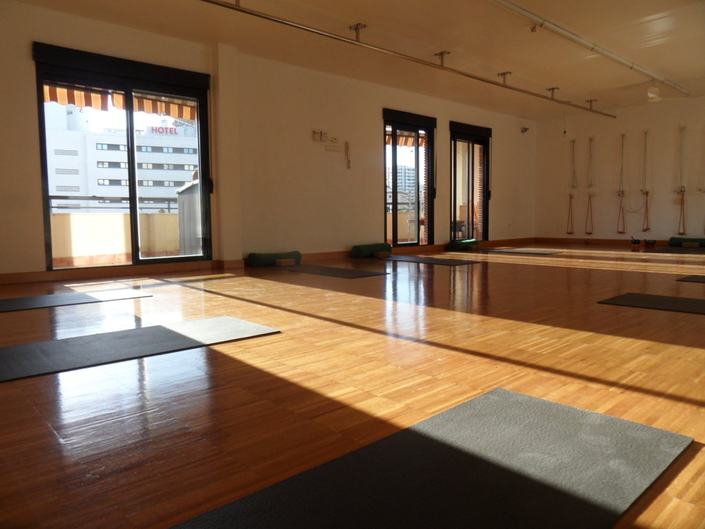 Sala de yoga con grandes ventanales y esterillas dispuestas sobre el suelo de madera